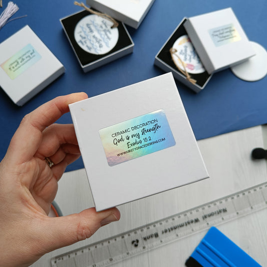 Hand holding a white box with decorative text on a blue surface with other similar boxes.