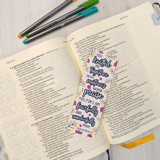Open book with colorful pens and a decorative bookmark on a light wooden surface