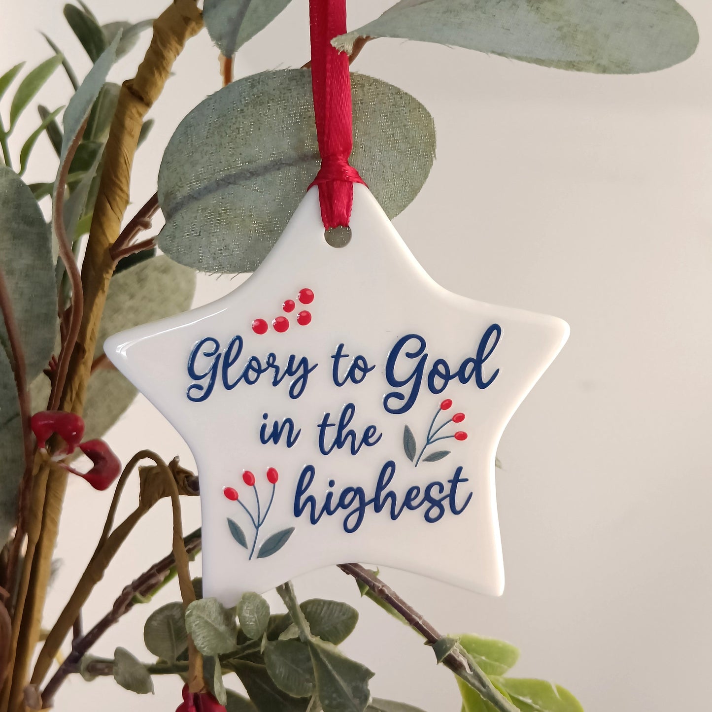Star-shaped ornament with 'Glory to God in the highest' text, hanging on a branch.