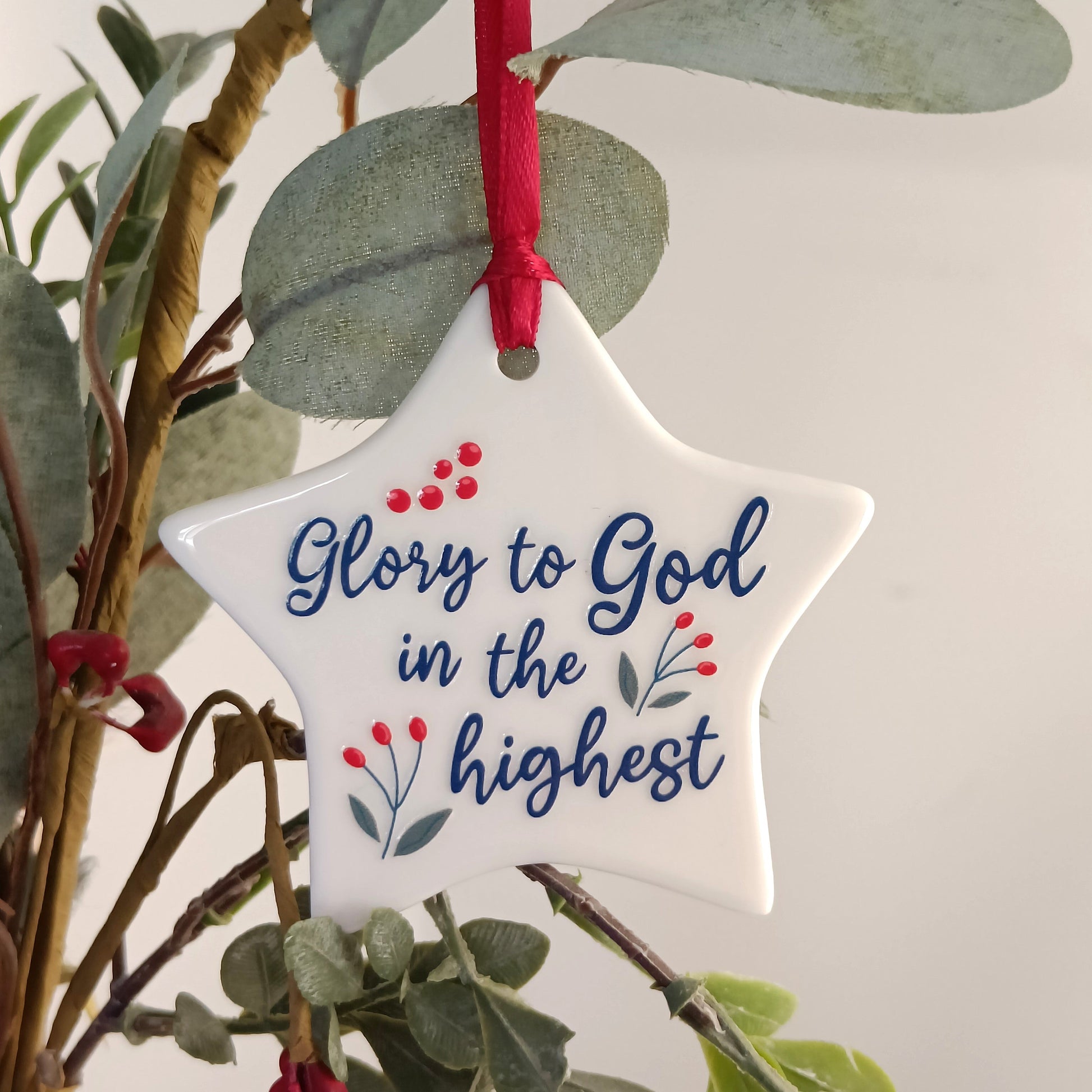 Star-shaped ornament with 'Glory to God in the highest' text, hanging on a branch.