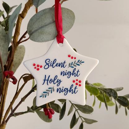 Star-shaped Christmas ornament with 'Silent night, Holy night' text hanging on a branch.