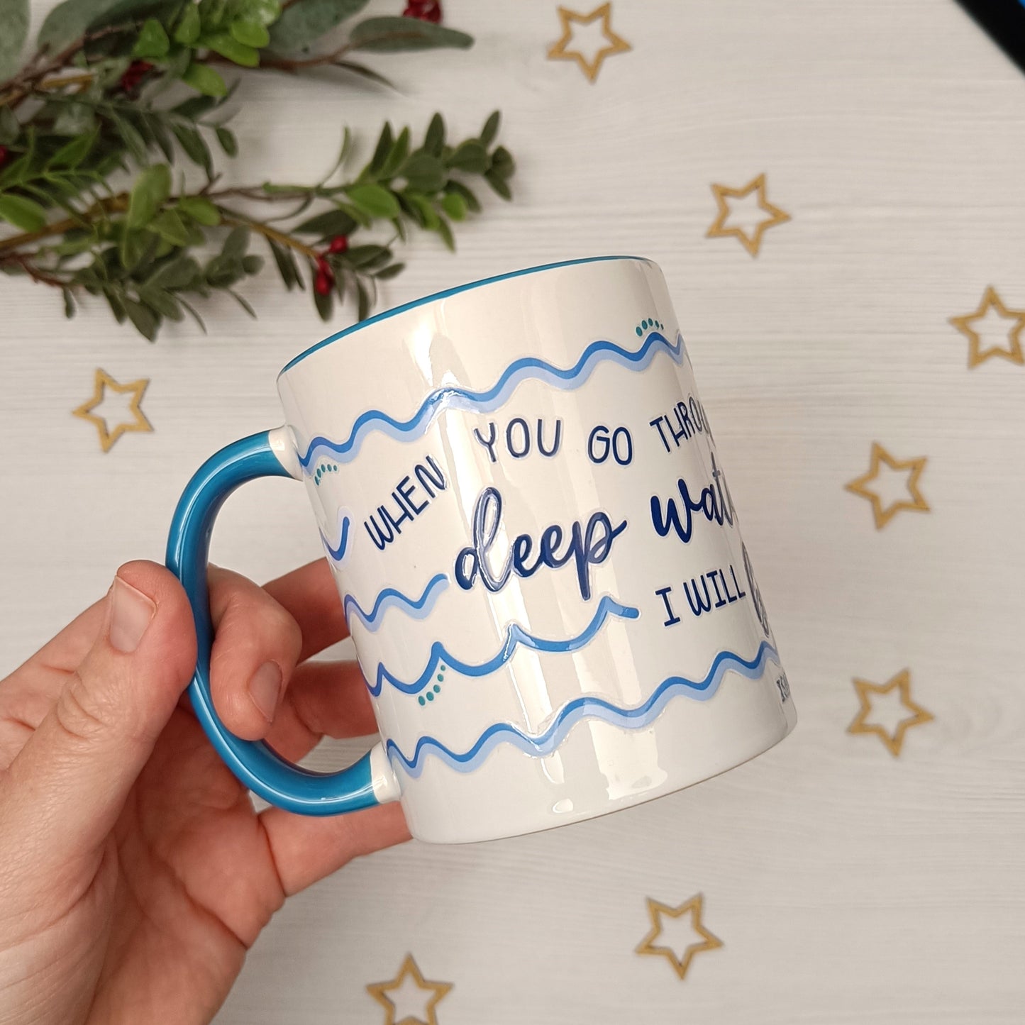 Mug with blue handle and text held by a hand on a decorative background