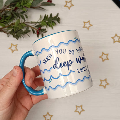 Mug with blue handle and text held by a hand on a decorative background