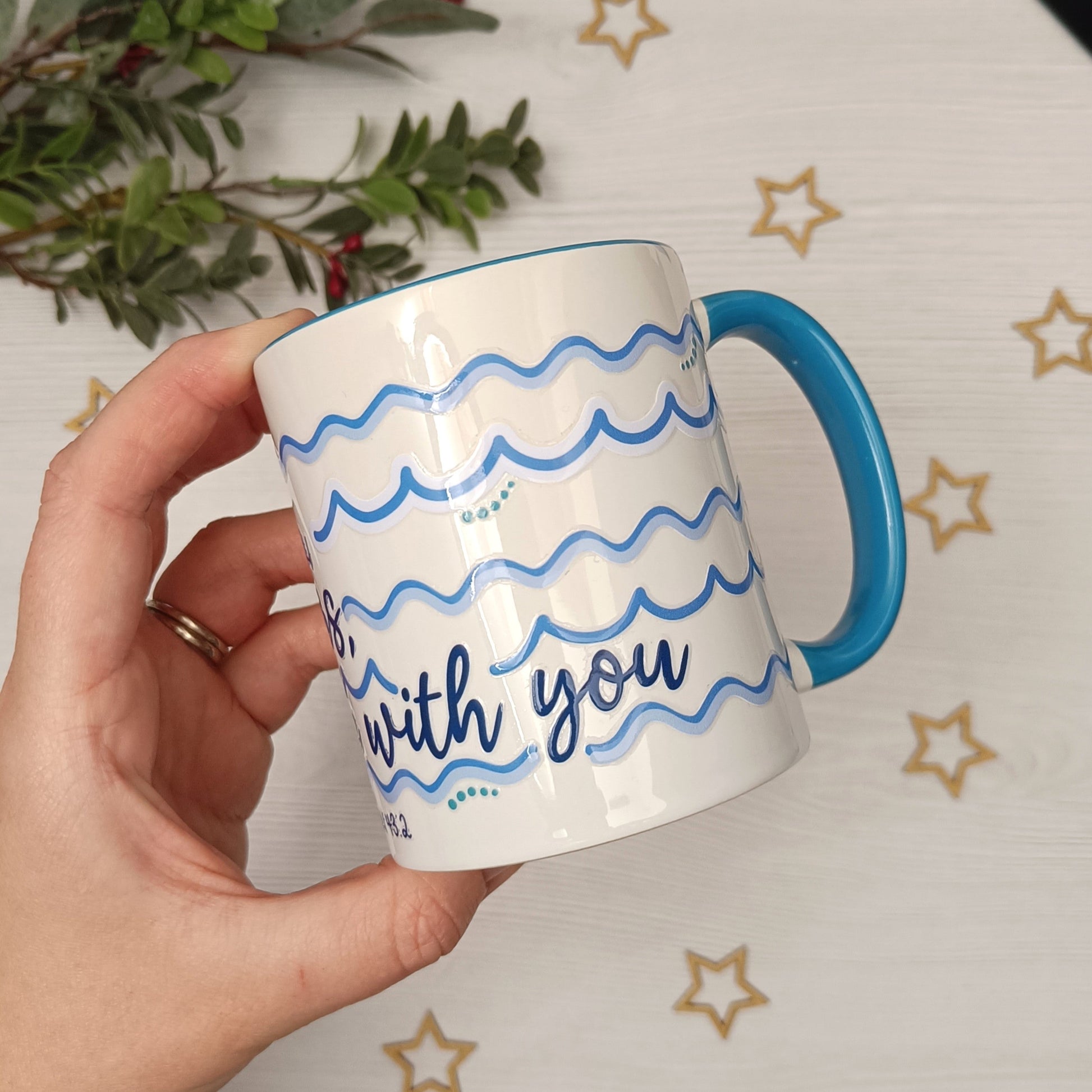 Hand holding a mug with blue handle and wavy text design against a star-patterned background