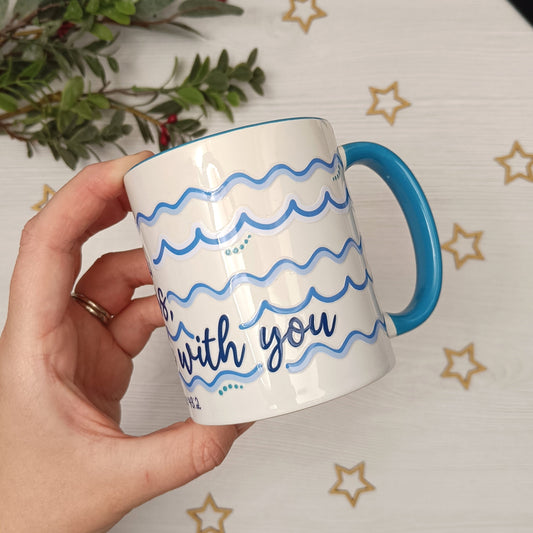 Hand holding a mug with blue handle and wavy text design against a star-patterned background