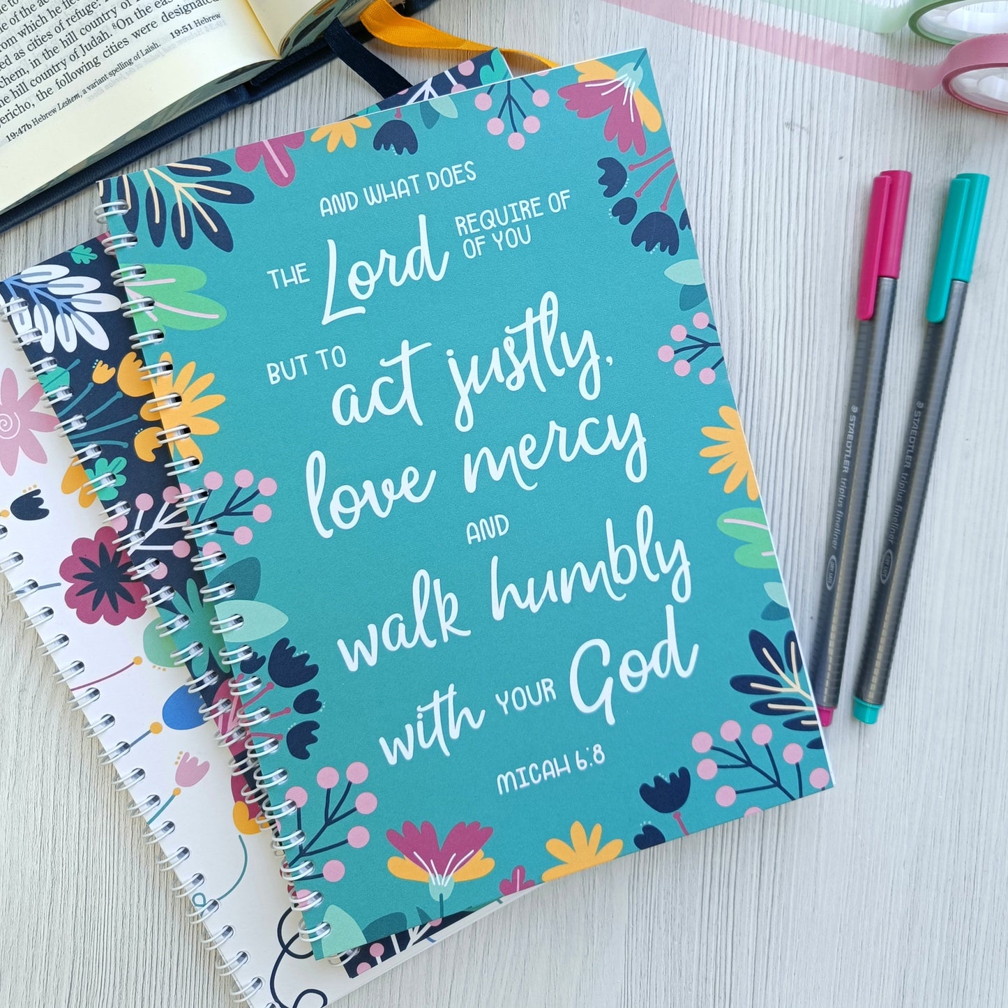 Notebook with colorful design and inspirational quote, placed on a surface with an open book and pens.