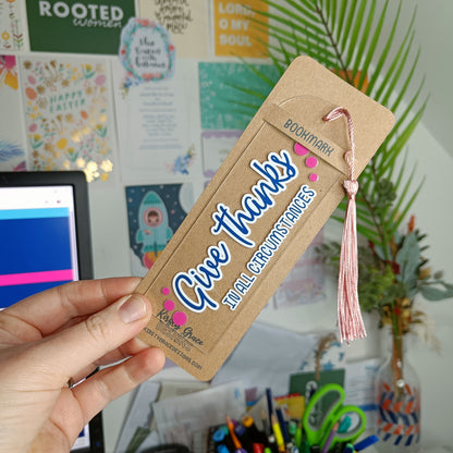 Bookmark with 'Give Thanks' text held by a hand in a colorful room setting.